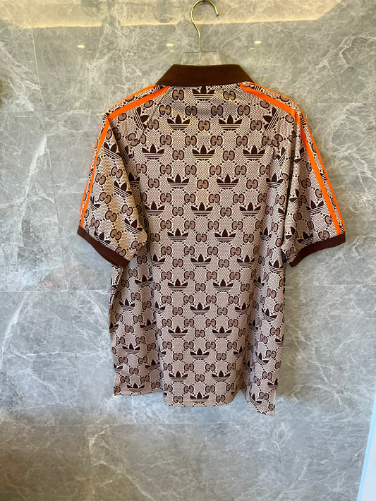 Polo marrón con monograma de Gucci x Adidas, ribete naranja y logotipos de trébol.