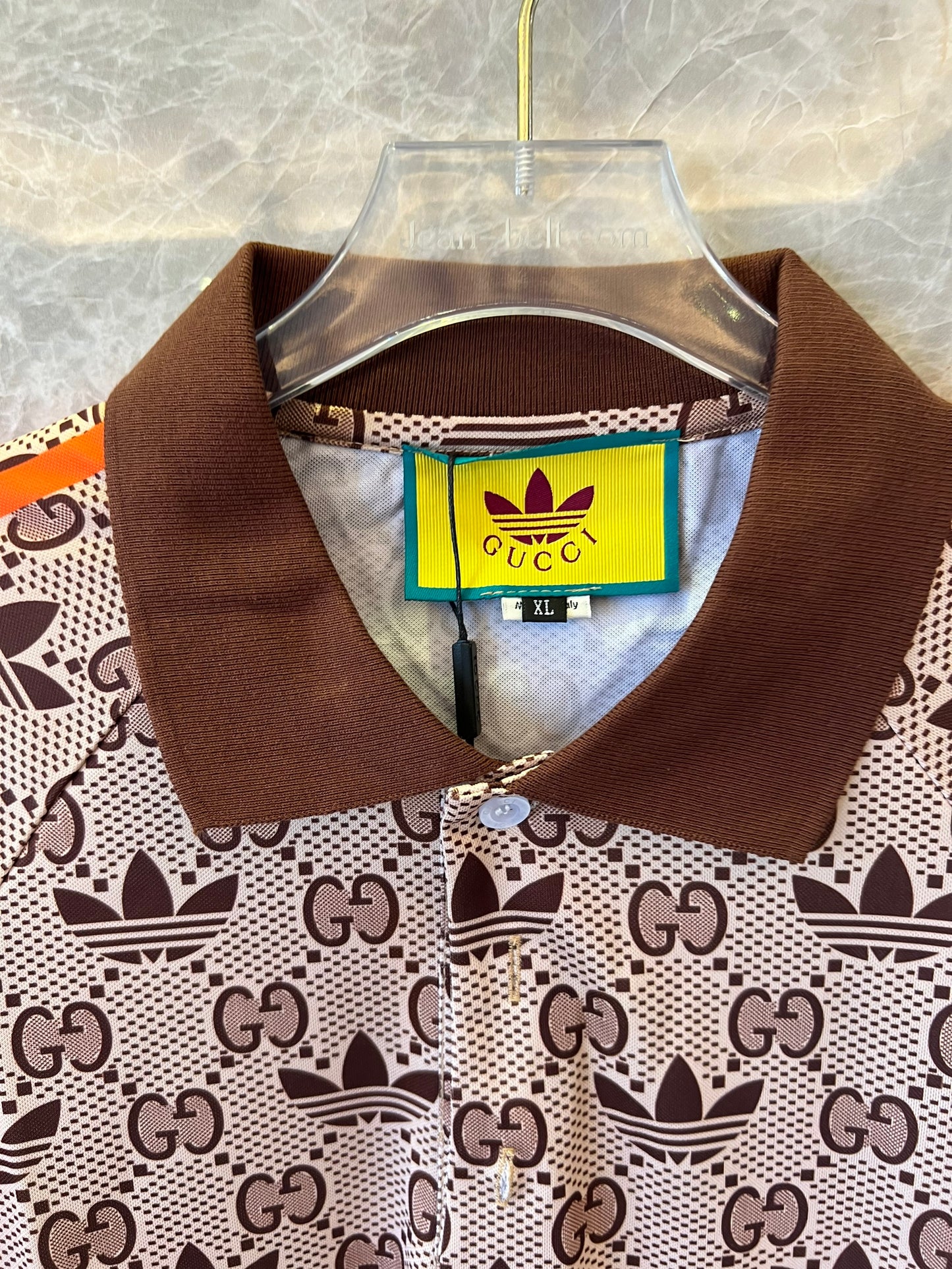 Polo marrón con monograma de Gucci x Adidas, ribete naranja y logotipos de trébol.