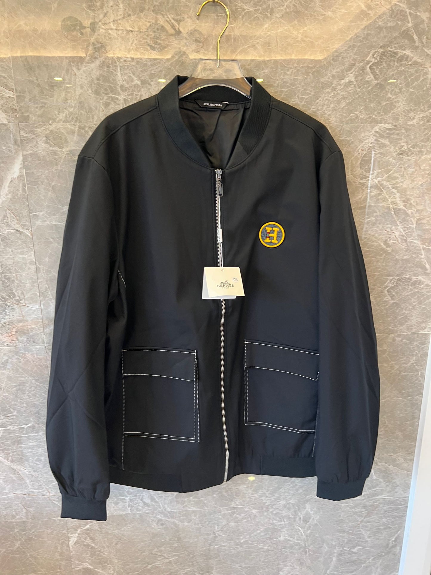 Chaqueta bomber de nailon negra de Hermès con parche del logotipo "H" amarillo.