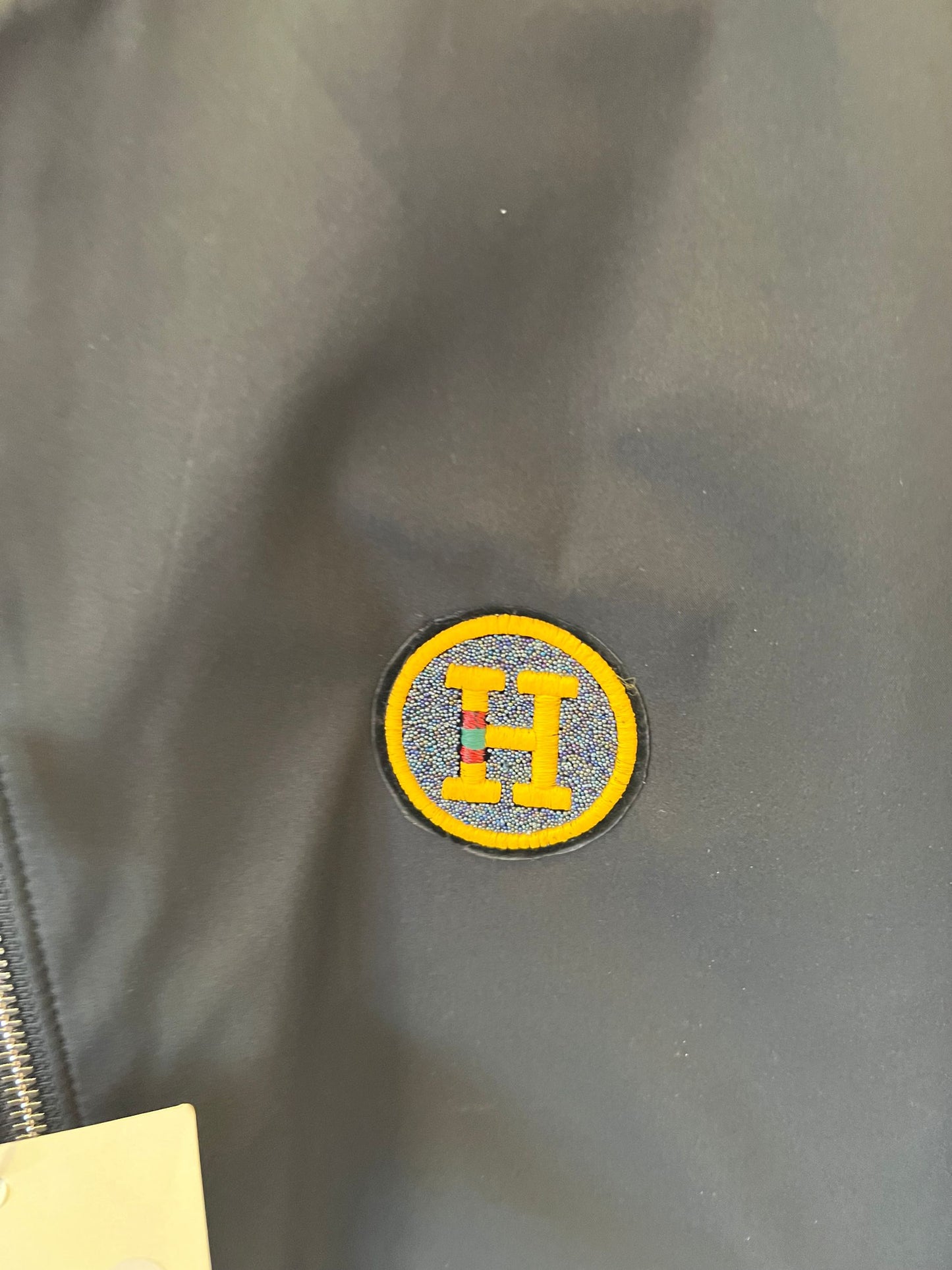 Chaqueta bomber de nailon negra de Hermès con parche del logotipo "H" amarillo.