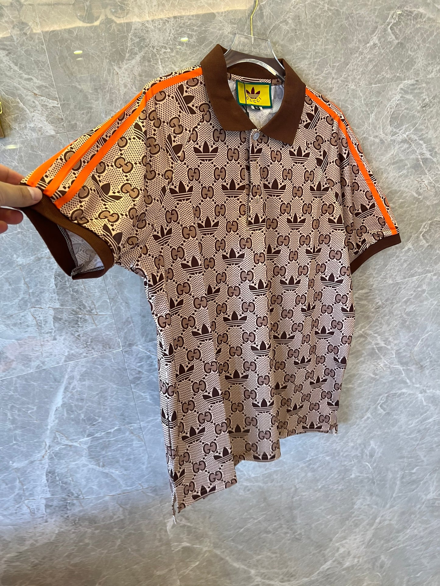 Polo marrón con monograma de Gucci x Adidas, ribete naranja y logotipos de trébol.