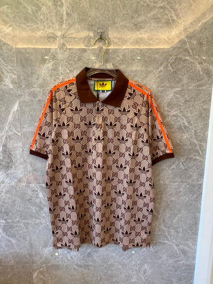 Polo marrón con monograma de Gucci x Adidas, ribete naranja y logotipos de trébol.