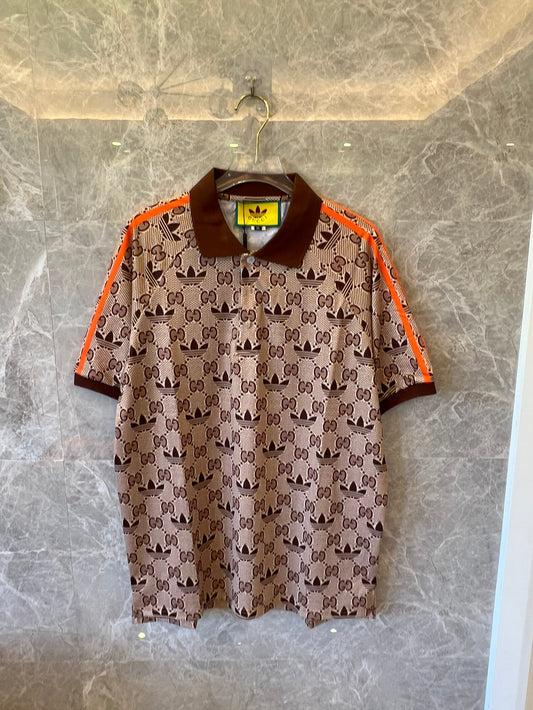 Polo marrón con monograma de Gucci x Adidas, ribete naranja y logotipos de trébol.
