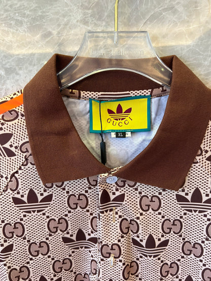 Polo marrón con monograma de Gucci x Adidas, ribete naranja y logotipos de trébol.